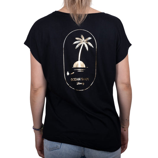Tee-shirt femme en coton biologique noir avec gros dessin palmier sur île et écriture « ocean shape Biarritz » couleur doré dans le dos, vu de dos sur mannequin femme 