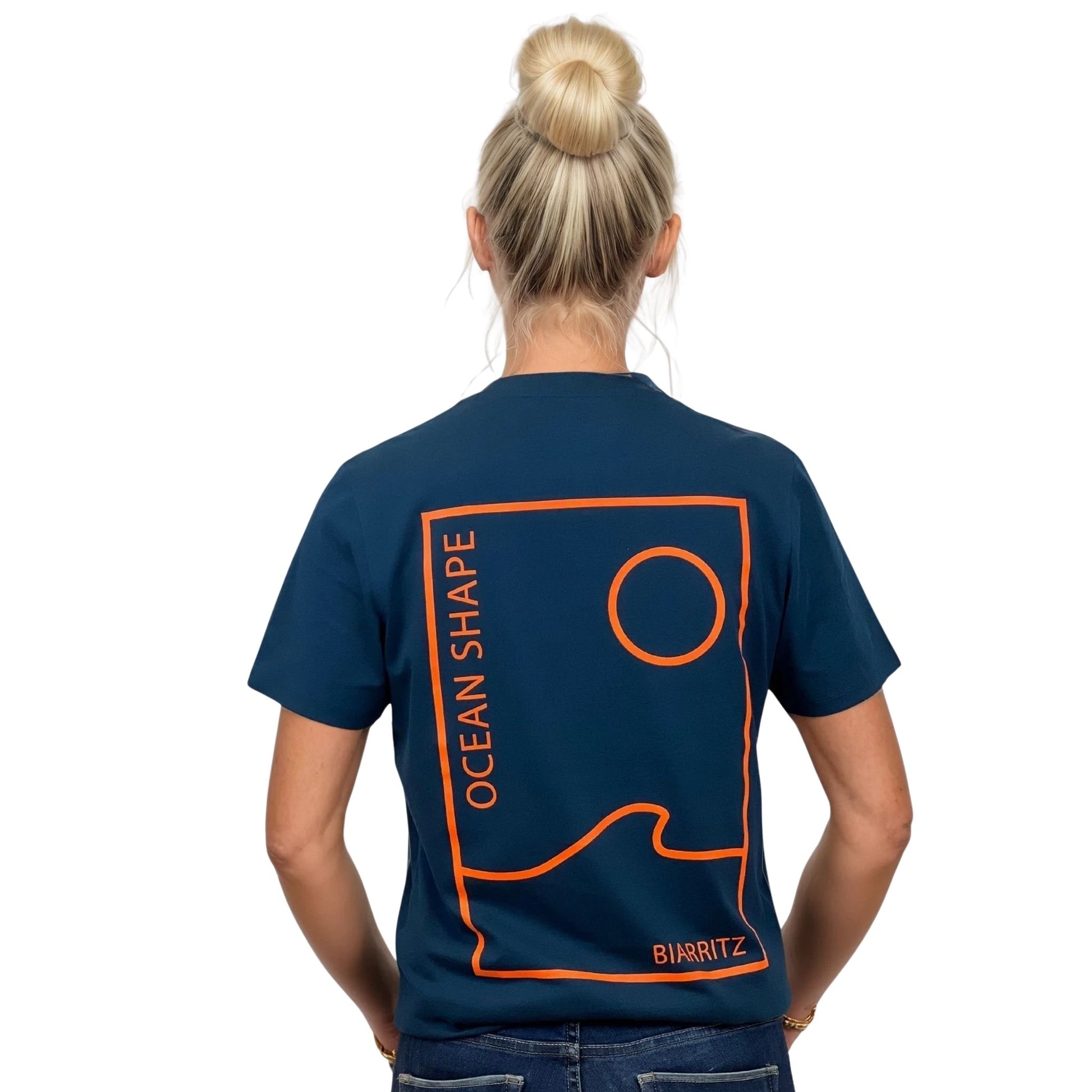 Tee-shirt unisexe bleu petrole en coton biologique avec grand encadré vague / soleil minimaliste + écriture "ocean shape Biarritz" orange fluo dans le dos, vu de dos sur mannequin femme.