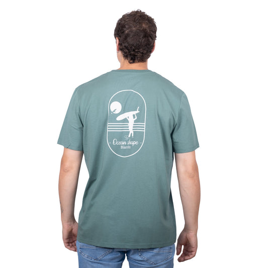 Tee-shirt unisexe vert sauge en coton biologique avec grand dessin de surfeuse qui marche de dos + écriture "Ocean Shape Biarritz" dans le dos, vu de dos sur mannequin homme
