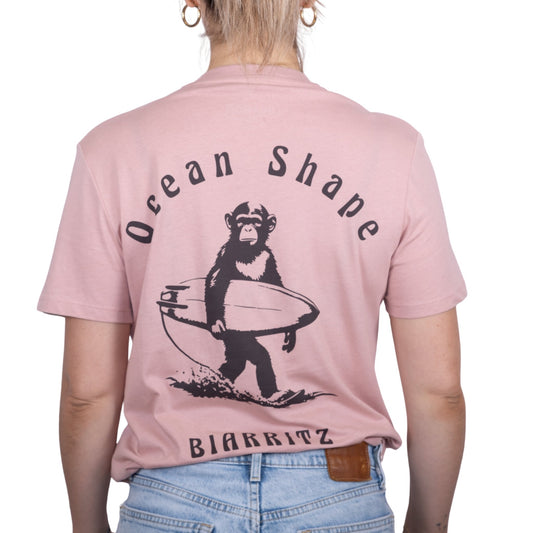 Tee-shirt unisexe rose pale en coton biologique avec gros dessin de singe surfeur et écriture « ocean shape Biarritz » marron foncé dans le dos, vu de dos sur mannequin femme