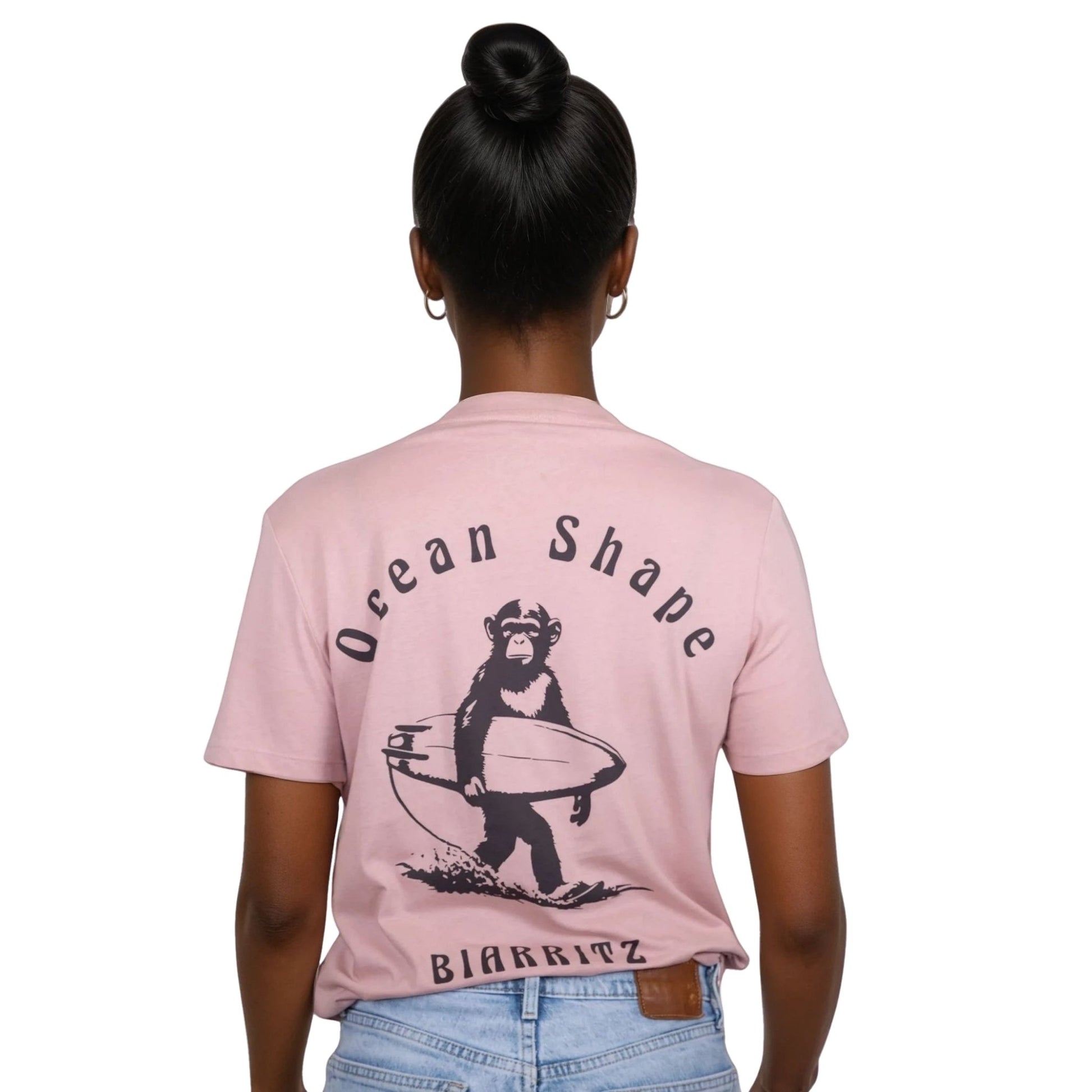 Tee-shirt unisexe rose pale en coton biologique avec gros dessin de singe surfeur et écriture « ocean shape Biarritz » marron foncé dans le dos, vu de dos sur mannequin femme