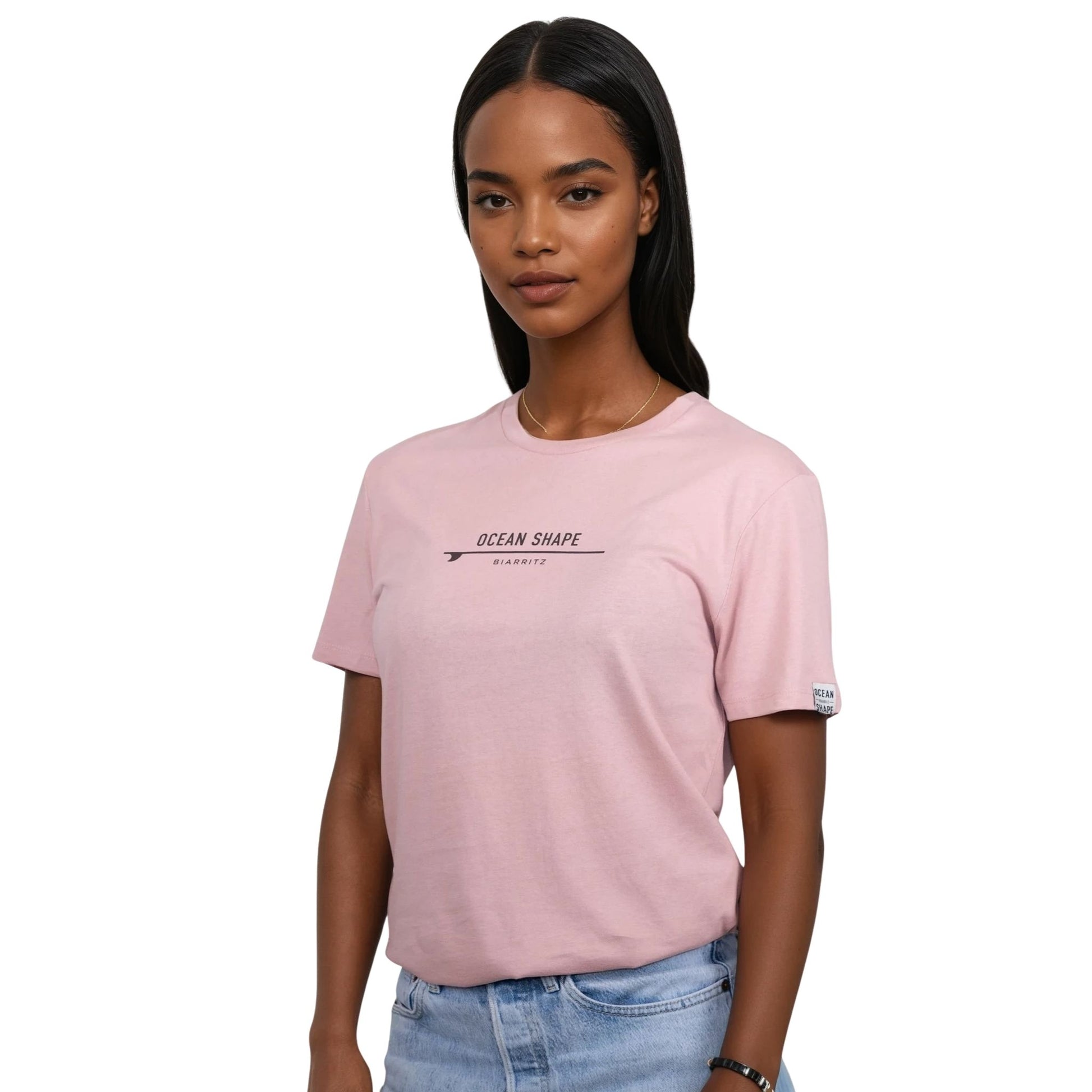 Tee-shirt unisexe rose pale en coton biologique avec petite signature "ocean shape Biarritz" sur surf marron foncé sur la poitrine, vu de face sur mannequin femme
