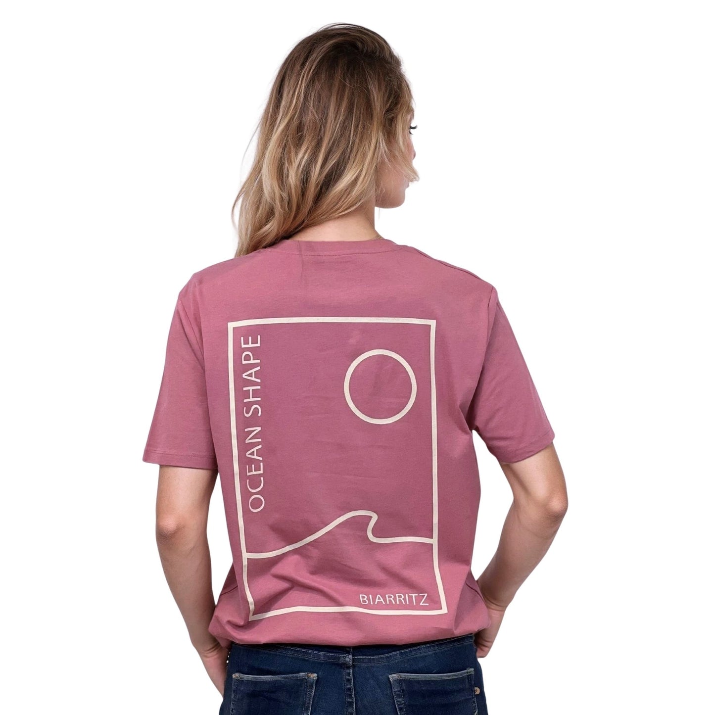 Tee-shirt unisexe rose foncé en coton biologique avec grand dessin vague / soleil minimaliste et écriture "ocean shape Biarritz" beige dans le dos, vu de dos sur mannequin femme.