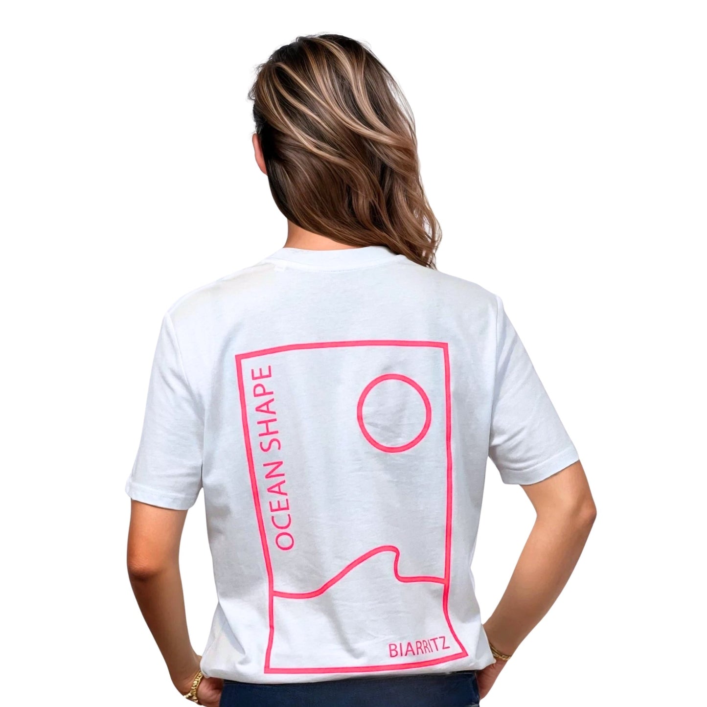 Tee-shirt unisexe blanc en coton biologique avec grand encadré vague / soleil minimaliste + écriture "ocean shape Biarritz" rose fluo dans le dos, vu de dos sur mannequin femme.