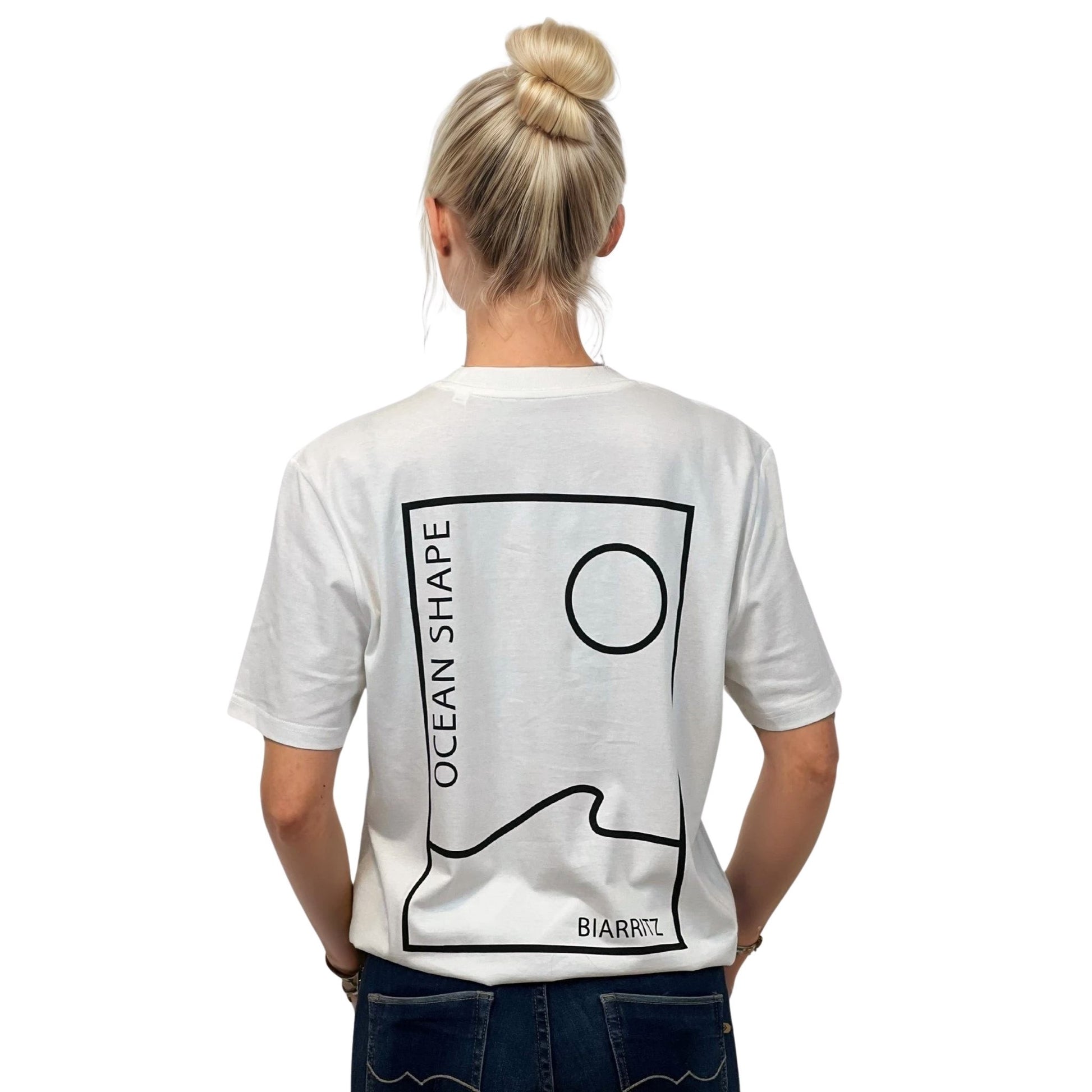 Tee-shirt unisexe blanc en coton biologique avec grand encadré vague / soleil minimaliste + écriture "ocean shape Biarritz" noir dans le dos, vu de dos sur mannequin femme.