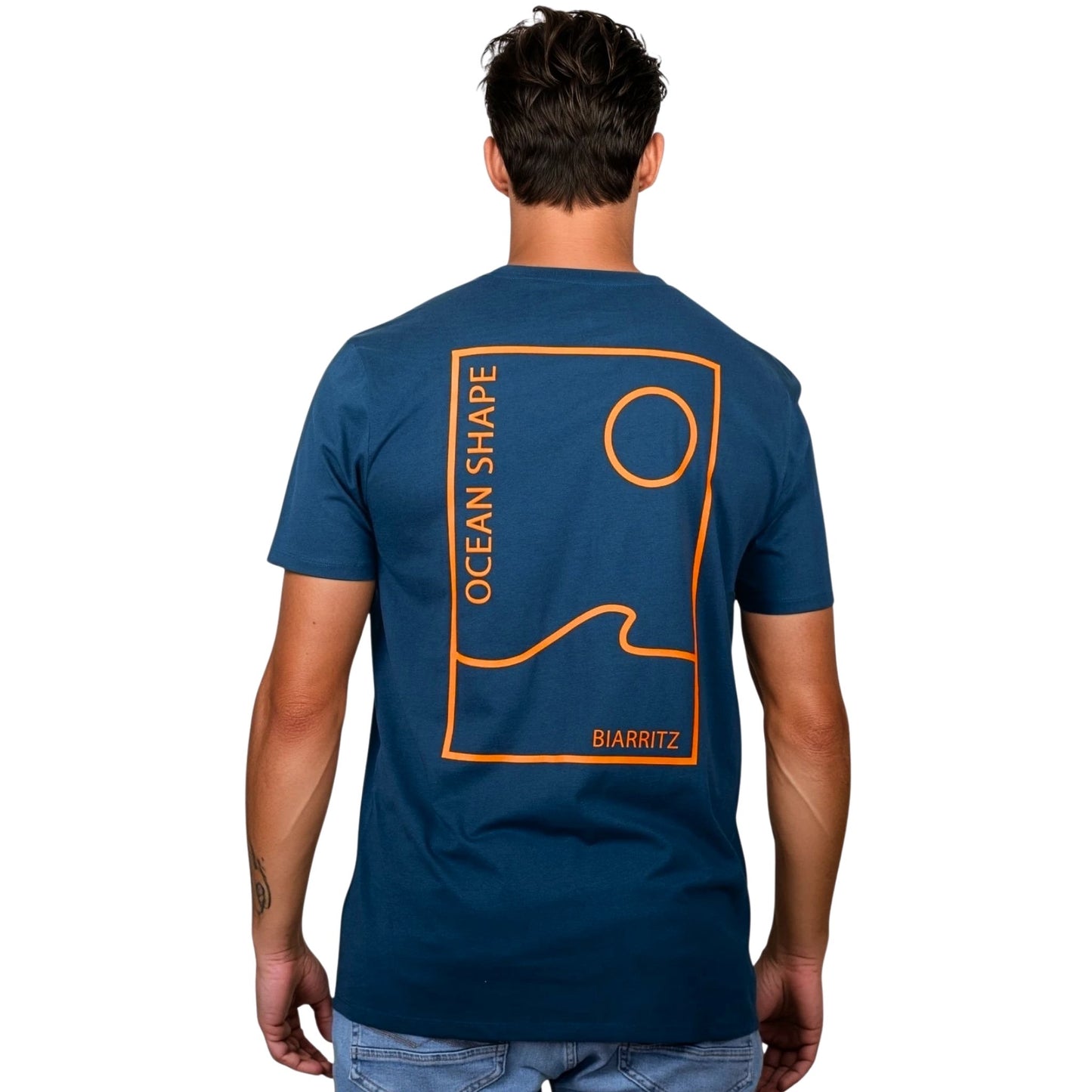 Tee-shirt unisexe bleu petrole en coton biologique avec grand encadré vague / soleil minimaliste + écriture "ocean shape Biarritz" orange fluo dans le dos, vu de dos sur mannequin homme.