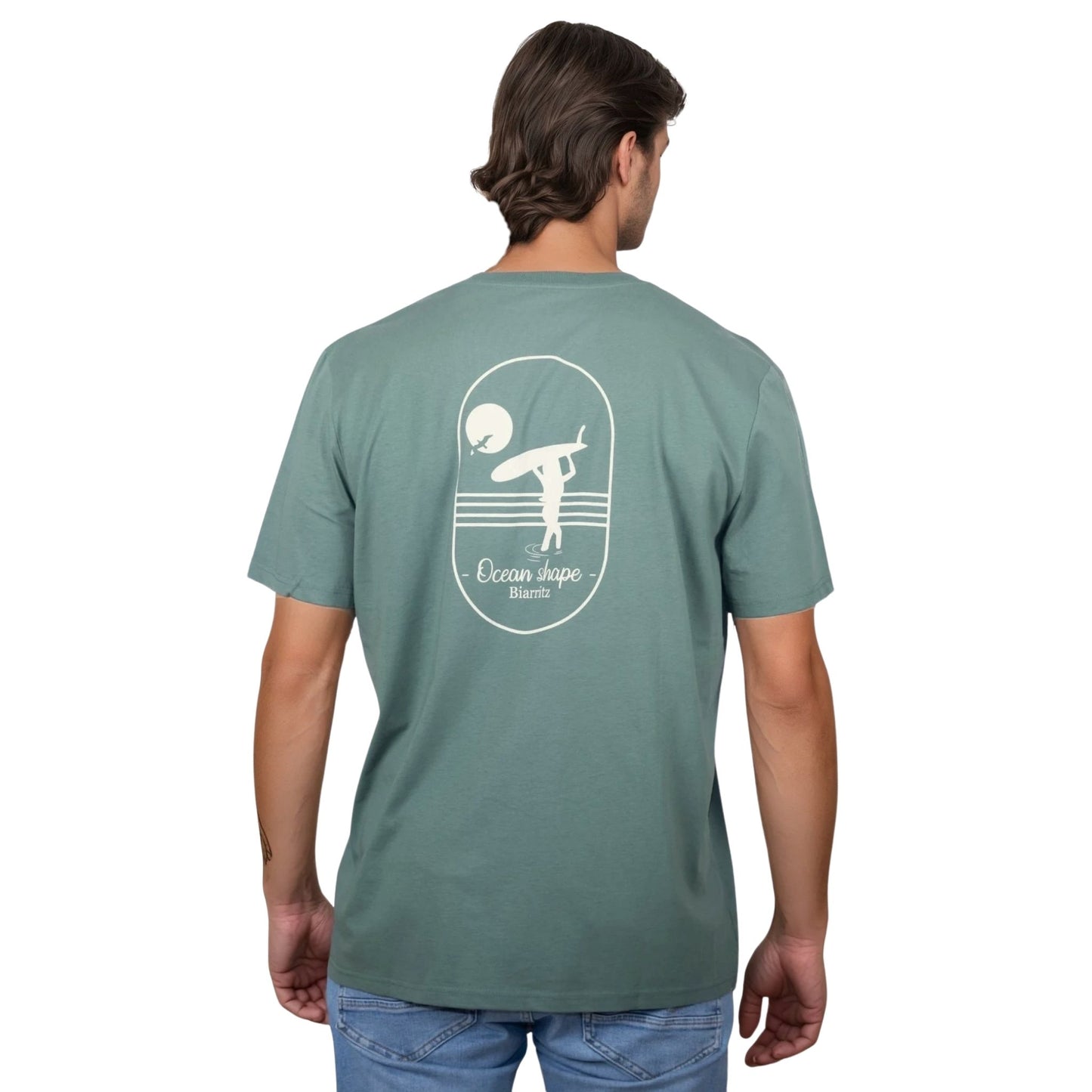 Tee-shirt unisexe vert sauge en coton biologique avec grand dessin de surfeuse qui marche + écriture "Ocean Shape Biarritz" écru dans le dos, vu de dos sur mannequin homme.
