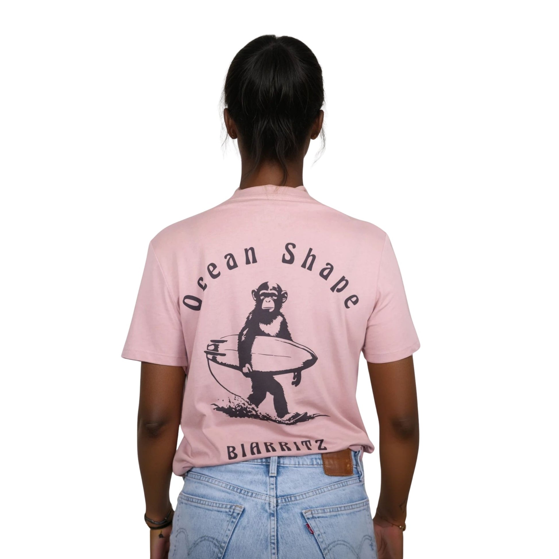 Tee-shirt unisexe rose pale en coton biologique avec gros dessin de singe surfeur et écriture « ocean shape Biarritz » marron foncé dans le dos, vu de dos sur mannequin femme