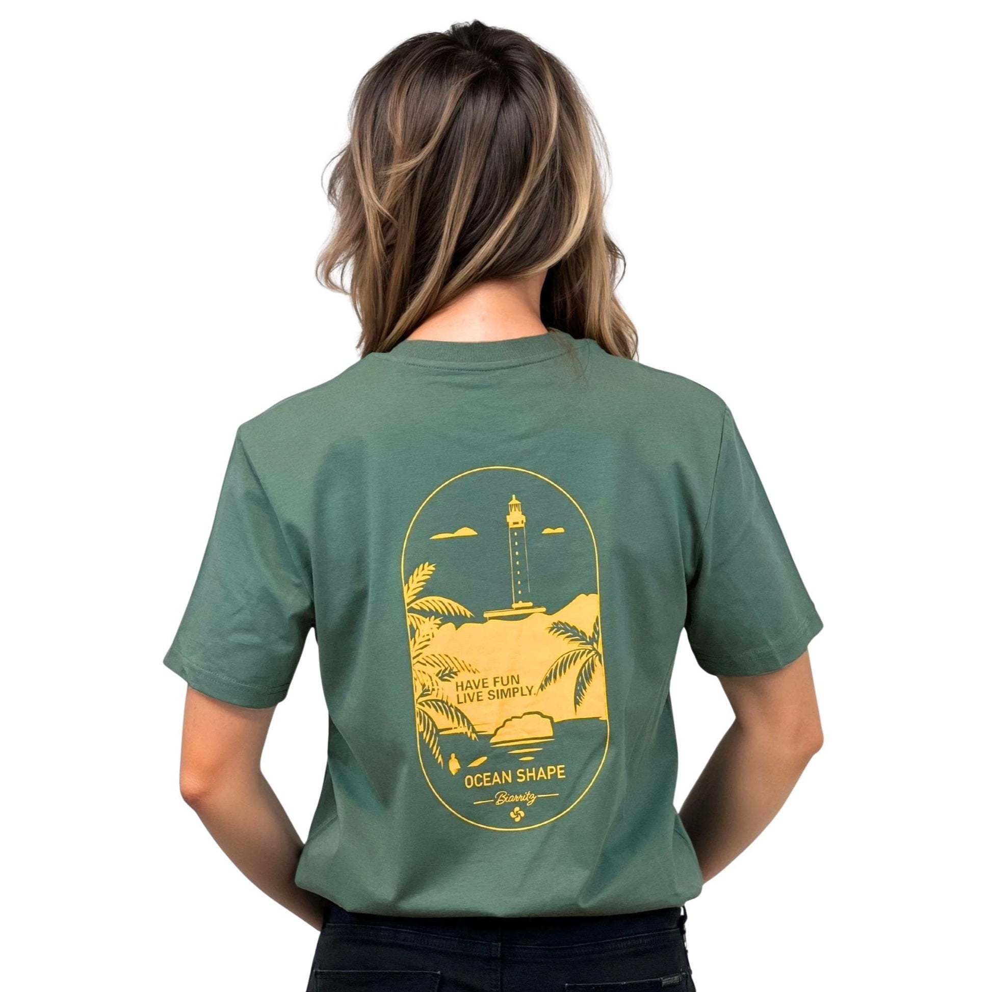 T-shirt unisexe vert sauge en coton biologique avec grand dessin phare de Biarritz jaune dans le dos, vu de dos sur mannequin femme.