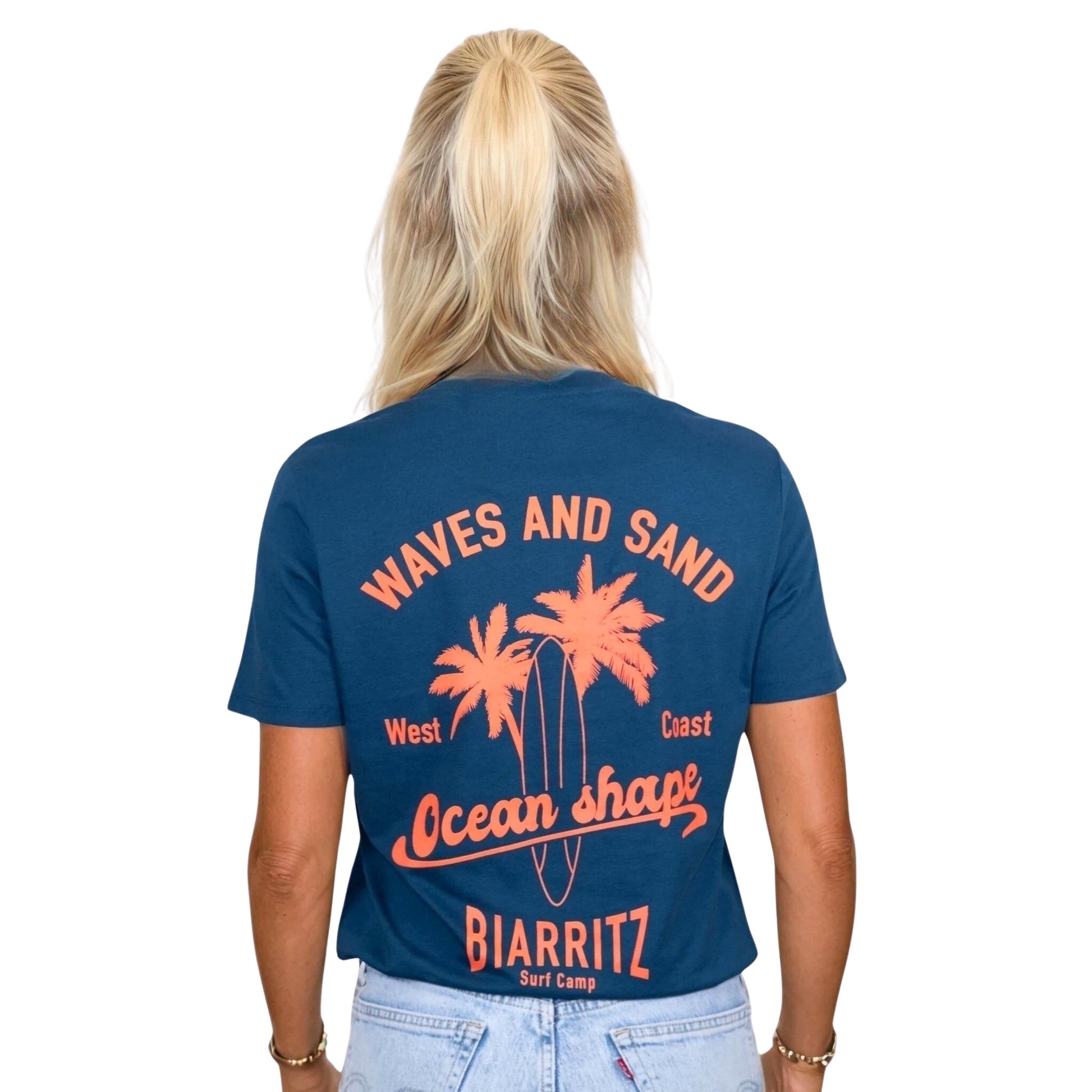 Tee-shirt unisexe en coton biologique bleu paon.
Grand dessin palmiers, planche de surf et écriture « ocean shape Biarritz » et « waves and sun » orange fluo dans le dos.
Vu de dos sur mannequin femme.