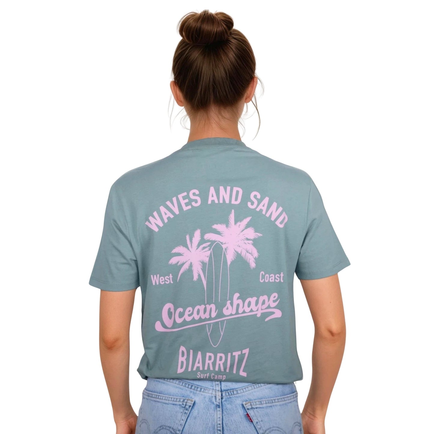 Tee-shirt unisexe vert sauge en coton biologique avec grand dessin de palmiers, planche de surf et écriture "Waves and Sand" et "Ocean Shape Biarritz" rose clair dans le dos, vu de dos sur mannequin femme.
