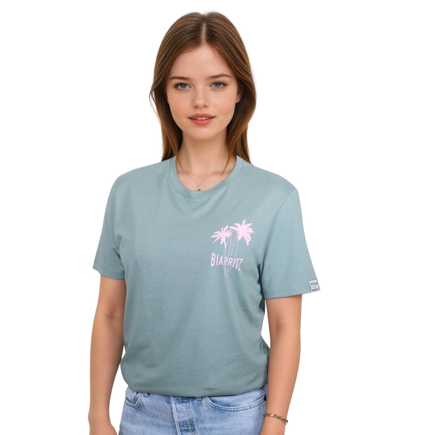 Tee-shirt unisexe vert sauge en coton biologique avec petit dessin de palmiers, planche de surf et écriture "Biarritz" rose clair sur la poitrine, vu de face sur mannequin femme.