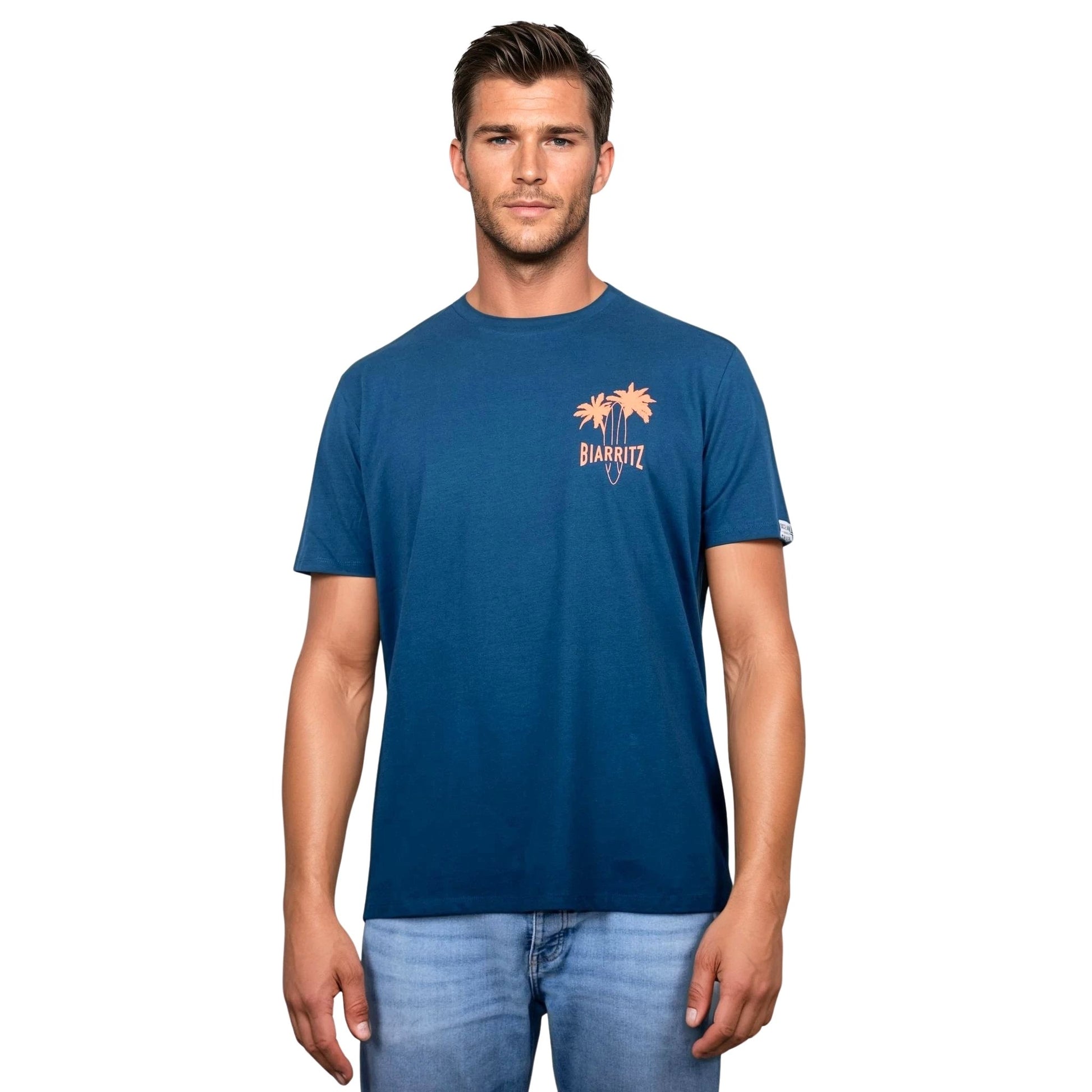 T-shirt unisexe en coton biologique bleu paon avec petit dessin palmiers, planche de surf et écriture « Biarritz » orange fluo sur la poitrine gauche, vu de face sur mannequin homme.