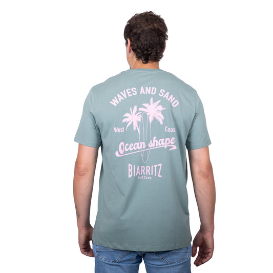 Tee-shirt unisexe vert sauge en coton biologique avec grand dessin de palmiers, planche de surf et écriture "Waves and Sand" et "Ocean Shape Biarritz" rose clair dans le dos, vu de dos sur mannequin homme