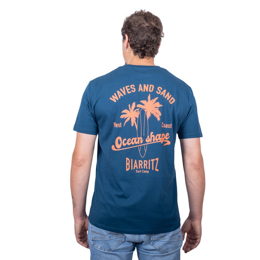 T-shirt unisexe en coton biologique bleu pétrole avec gros dessin palmiers, planche de surf et écriture « ocean shape Biarritz » et « waves and sun » en orange fluo dans le dos, vu de dos sur mannequin homme 